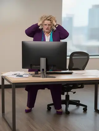 TAG totally stressed out hands on head grimous on face behind a desk with a computer on both hands on head